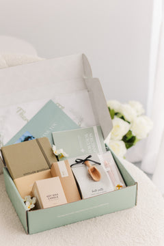 Open box containing stationery items on a light surface with flowers in the background