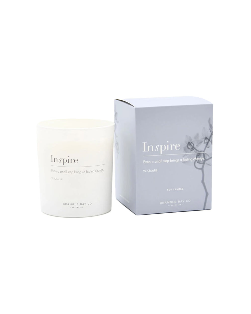 A white glass candle jar labeled 'Inspire' stands next to its light gray packaging box, both printed with the same elegant text and a subtle floral line drawing. The brand 'BRAMBLE BAY CO.