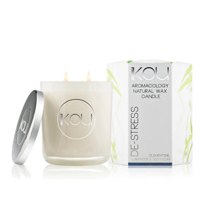 A KOU brand natural wax candle in a frosted glass jar with a silver lid leaning beside it, next to its white packaging box with green leaf accents, on a clean white background.