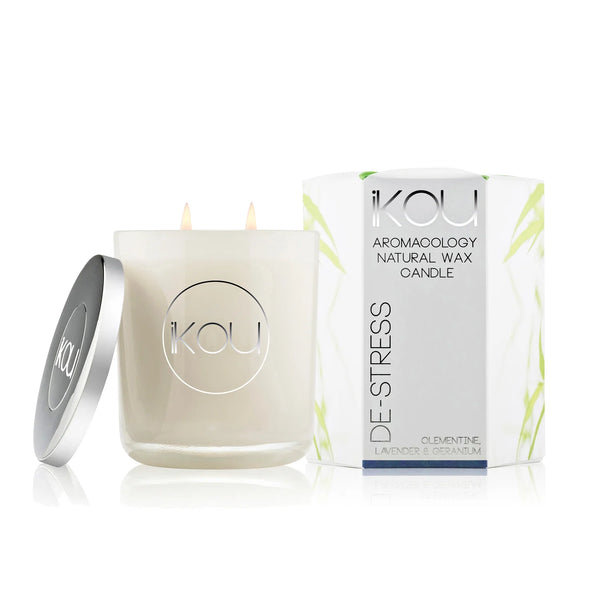 A KOU brand natural wax candle in a frosted glass jar with a silver lid leaning beside it, next to its white packaging box with green leaf accents, on a clean white background.