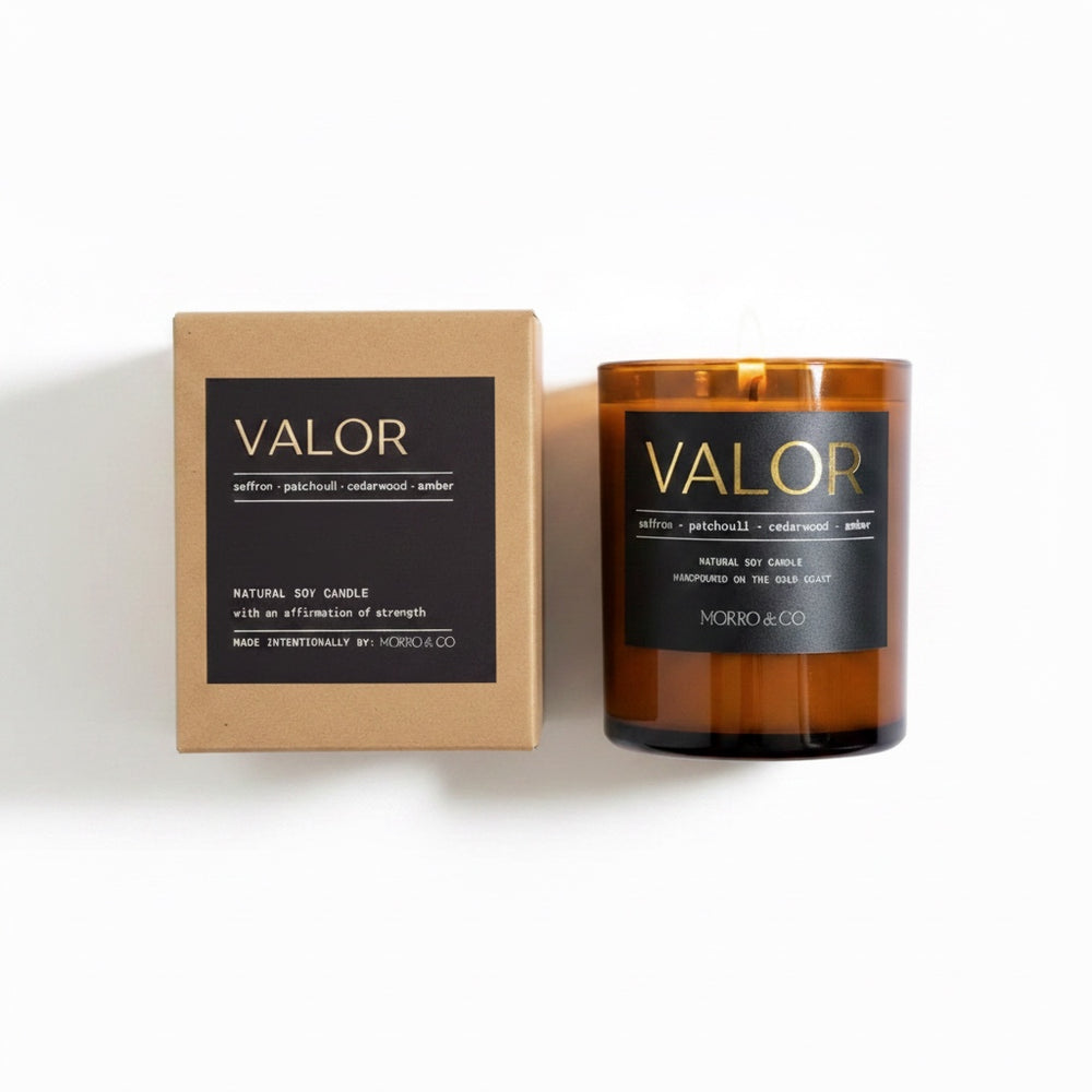 An amber glass jar candle next to its kraft paper packaging box, both featuring a black label with gold lettering that reads 'VALOR' and 'MORRO & CO'.