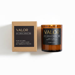 An amber glass jar candle next to its kraft paper packaging box, both featuring a black label with gold lettering that reads 'VALOR' and 'MORRO & CO'.