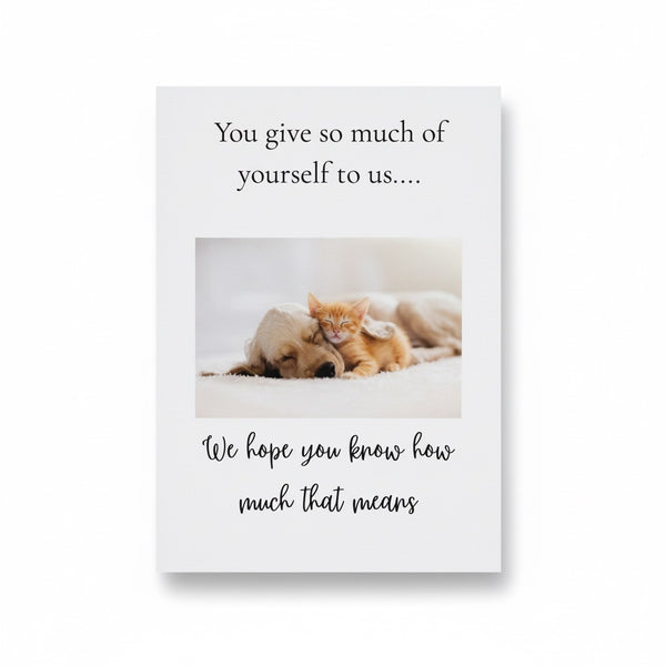 A square greeting card or print with a white background, featuring a photo of a small orange kitten resting on top of a light-colored dog. The text above reads, 'You give so much of yourself to us.