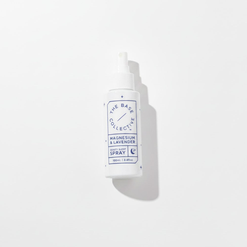 A white plastic spray bottle with a white cap, featuring a blue and white label that reads 'THE BASE COLLECTIVE' and 'MAGNESIUM & LAVENDER SPRAY'. The bottle is photographed on a clean white background with a soft shadow to the right.
