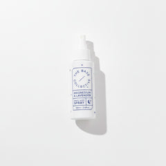 A white plastic spray bottle with a white cap, featuring a blue and white label that reads 'THE BASE COLLECTIVE' and 'MAGNESIUM & LAVENDER SPRAY'. The bottle is photographed on a clean white background with a soft shadow to the right.