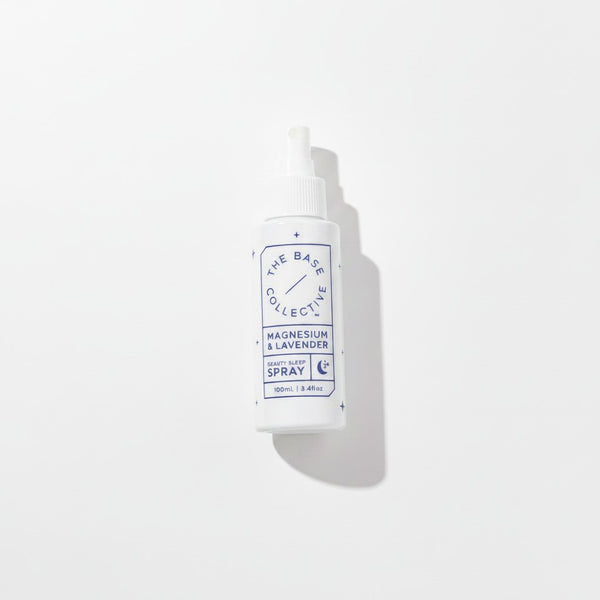 A white plastic spray bottle with a white cap, featuring a blue and white label that reads 'THE BASE COLLECTIVE' and 'MAGNESIUM & LAVENDER SPRAY'. The bottle is photographed on a clean white background with a soft shadow to the right.