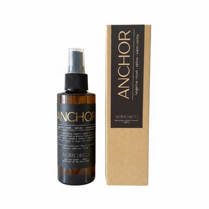 An amber glass spray bottle labeled ANCHOR by MORRO&CO next to its kraft paper packaging box, on a plain white background.