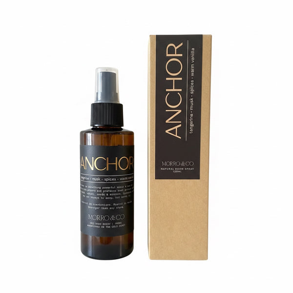 An amber glass spray bottle labeled ANCHOR by MORRO&CO next to its kraft paper packaging box, on a plain white background.