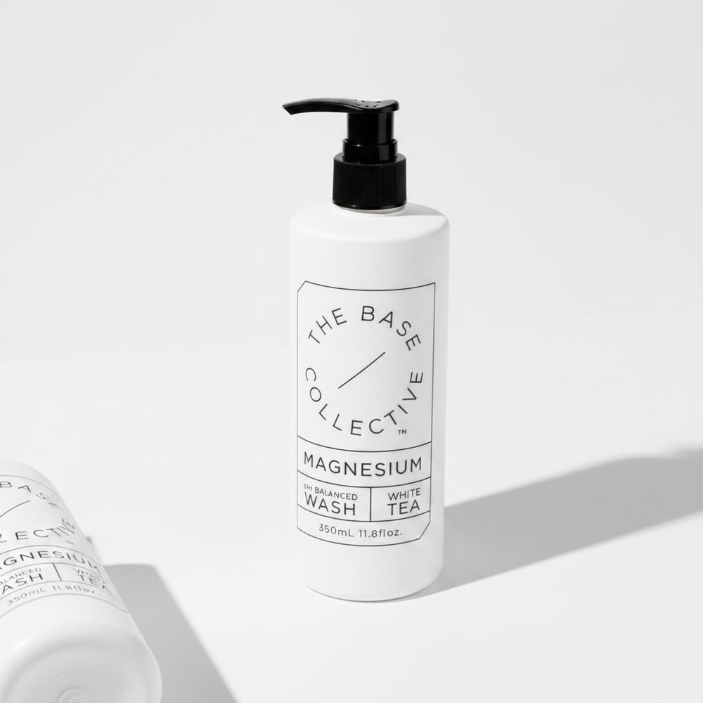 A white pump bottle of The Base Collective Magnesium Enhanced Wash with White Tea, shown on a clean white background with a second bottle partially visible in the foreground.