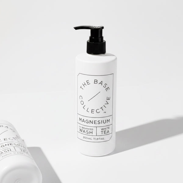 A white pump bottle of The Base Collective Magnesium Enhanced Wash with White Tea, shown on a clean white background with a second bottle partially visible in the foreground.