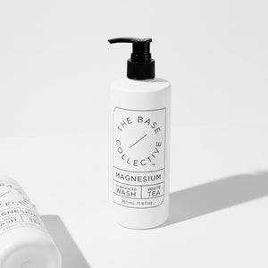 A white pump bottle of The Base Collective Magnesium Enhanced Wash with White Tea, shown on a clean white background with a second bottle partially visible in the foreground.