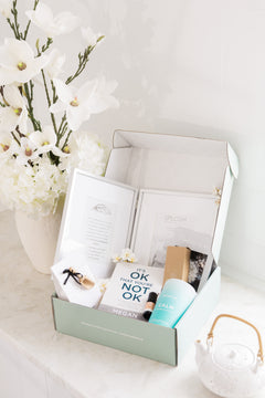 Gift box with grief products and a book on a white surface with flowers in the background