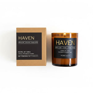 A brown amber glass jar candle next to its kraft paper packaging box, both featuring black labels with gold lettering for the brand Haven and scent 'Rich Cocoa - Creamy Vanilla'.