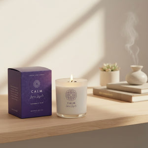 Bramble Bay Calm lemongrass and myrrh crystal soy candle burning beside its purple box, with a person meditating softly in the background.