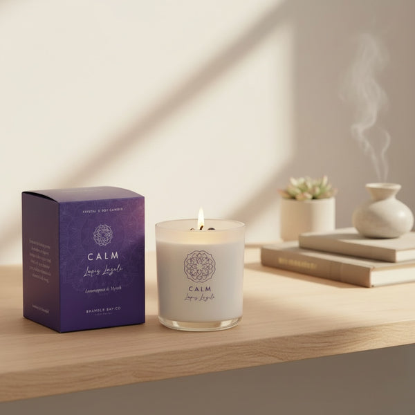 Bramble Bay Calm lemongrass and myrrh crystal soy candle burning beside its purple box, with a person meditating softly in the background.