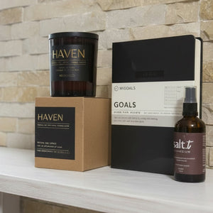 Candle, box, and bottle on a white surface with stone wall background