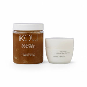 Two skincare products from the brand iKOU on a clean white background: a clear jar of Organic Body Buff in orange and jojoba oil, and a white jar of De-Stress Organic Body Crème.