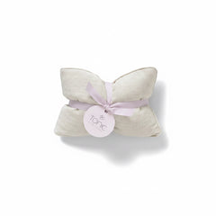 A folded cream-colored textured fabric pillow or cushion tied with a light lavender ribbon and a round white paper tag that reads 'tonic', set against a plain white background.
