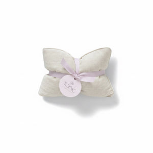 A folded cream-colored textured fabric pillow or cushion tied with a light lavender ribbon and a round white paper tag that reads 'tonic', set against a plain white background.