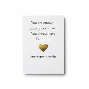 A white rectangular card or plaque with printed text reading 'You are enough, exactly as you are. You always have been.