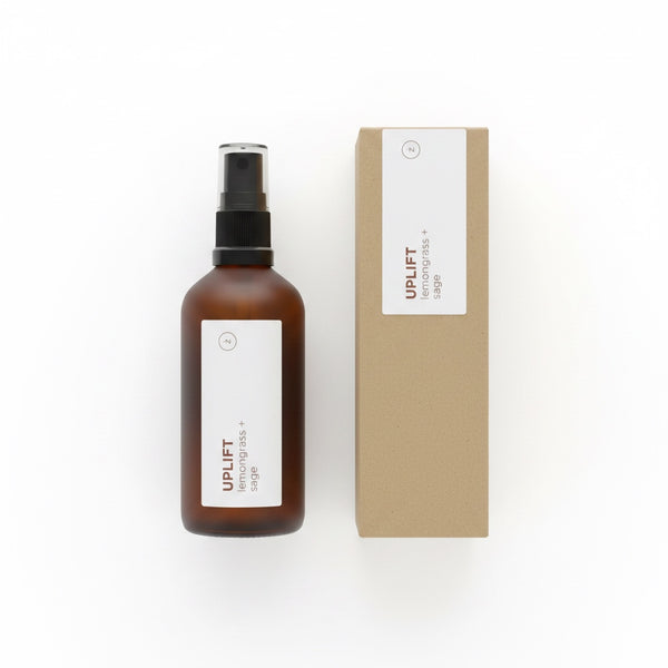 An amber glass spray bottle with a black pump and a white label next to its brown kraft paper box, both featuring the brand name UPLIFT.