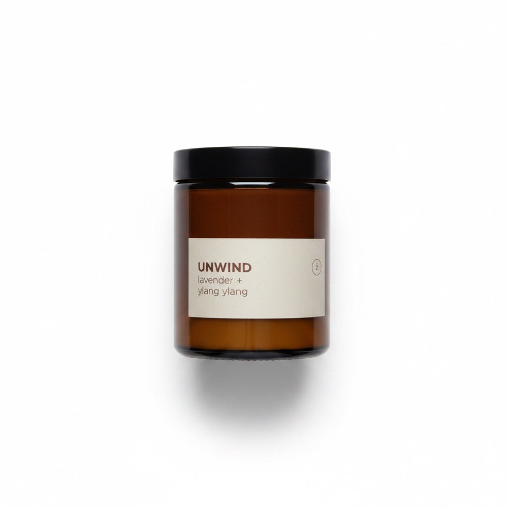 An amber glass jar candle with a black lid and a cream label next to its beige packaging box, on a clean white background.