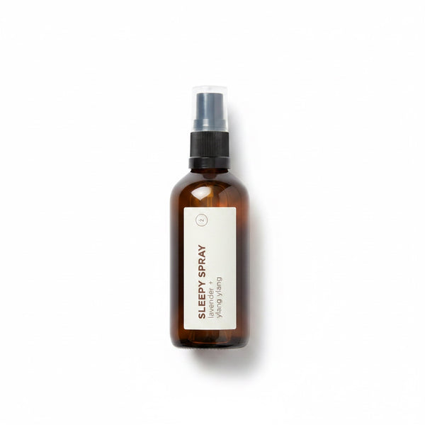An amber glass spray bottle labeled 'SLEEPY SPRAY' by Yang Wang, featuring a black spray nozzle and a minimalist white label, set against a clean white background with a soft shadow.